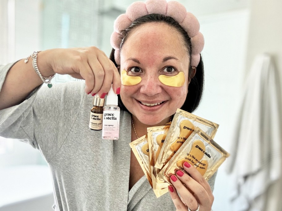 woman wearing gold under eye patches and holding up skincare serums and more eye patches