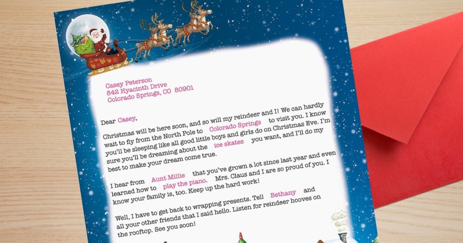 letter from Santa on a piece of paper with Santa and his reindeer flying thru the night sky next to a red envelope on a desk