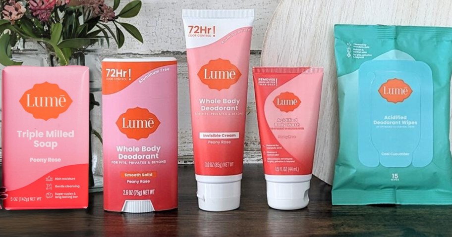 4 pink and white Lume soap, stick deodorant, cream deodorant, body wash small tube, and green pack of body wipes on a counter