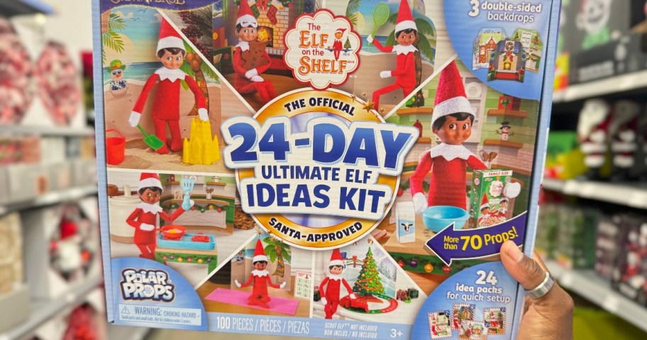 hand holding a colorful box with Elf on the Shelf scenes on it. The box says Elf on the Shelf 34-Day Ultimate Ideas Kit