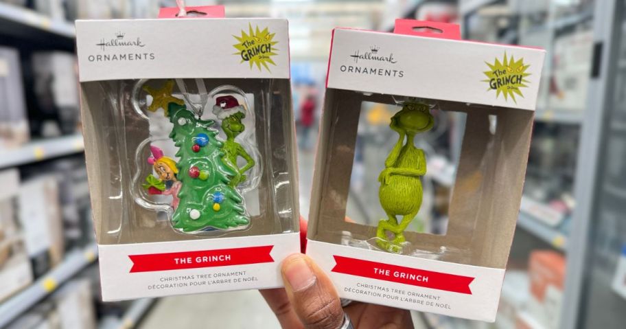 Hand holding up two Hallmark Grinch ornaments at Walmart