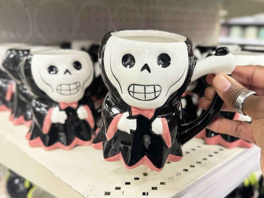 hand holding up a black, white, and pink grim reaper coffee mug