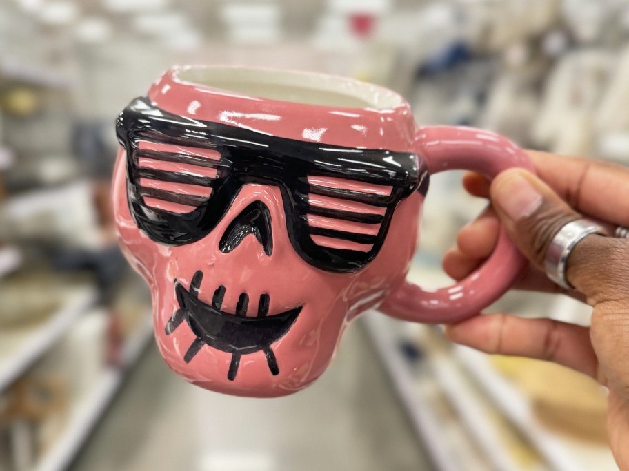 hand holding up a pink skull coffee mug wearing sunglasses