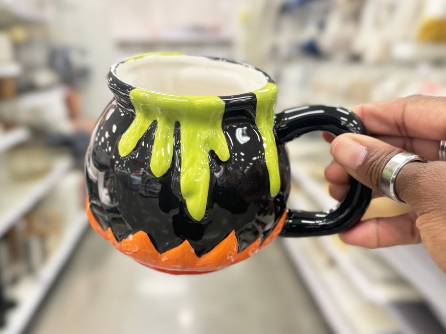 hand holding up a halloween cauldron coffee mug