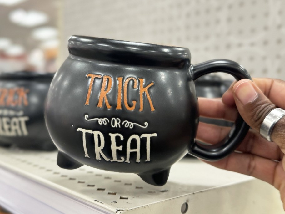 hand holding up a black cauldron mug that says "trick or treat"