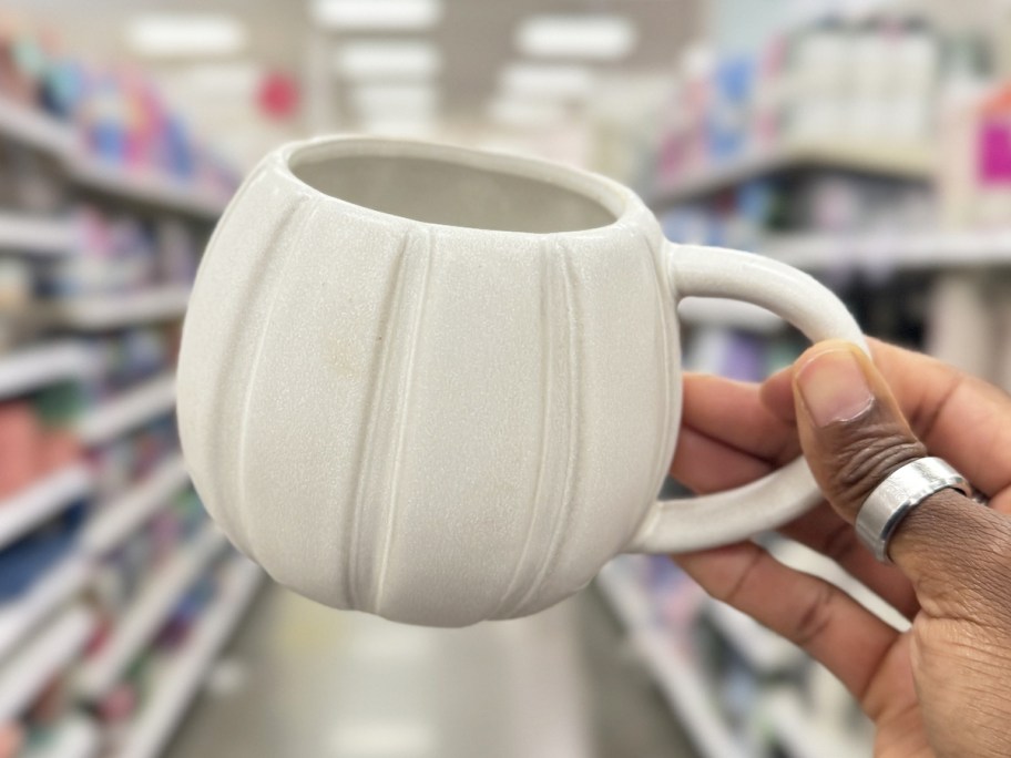hand holding up a white pumpkin mug in store