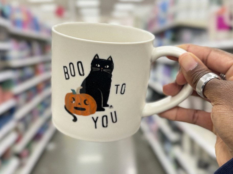 hand holding up a white coffee mug with a black cat and pumpkin that says "boo to you"
