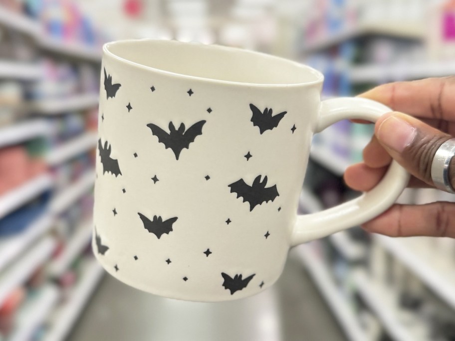 hand holding up a white coffee mug with black bat print