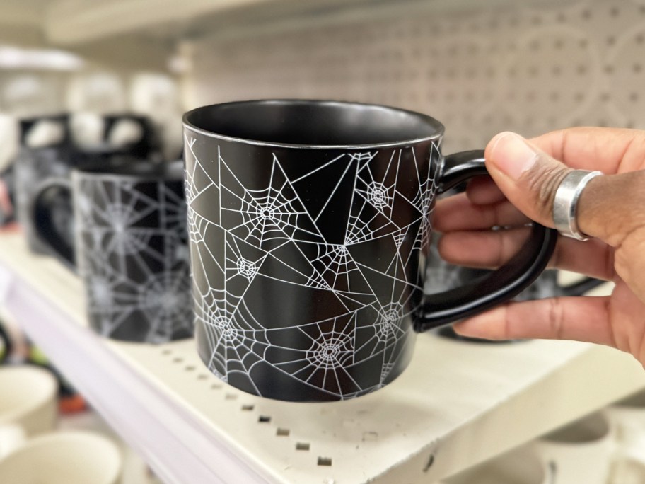 hand holding up a black and white spiderweb print coffee mug