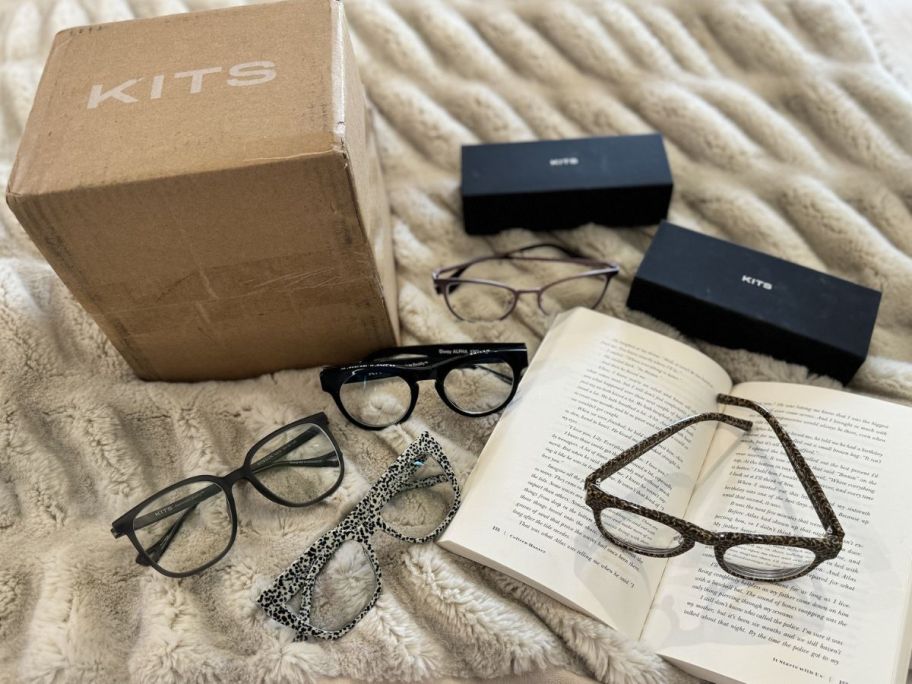 Several pairs of kits glasses on a bed with a book and a shipping box