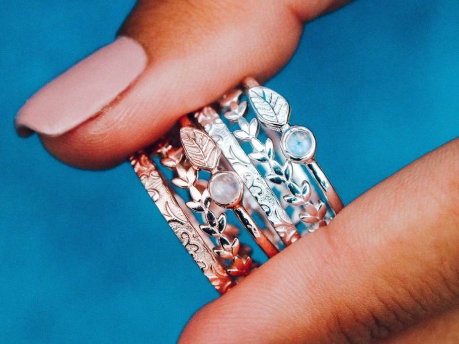 a womans hand holding rose gold and silver ring stacks