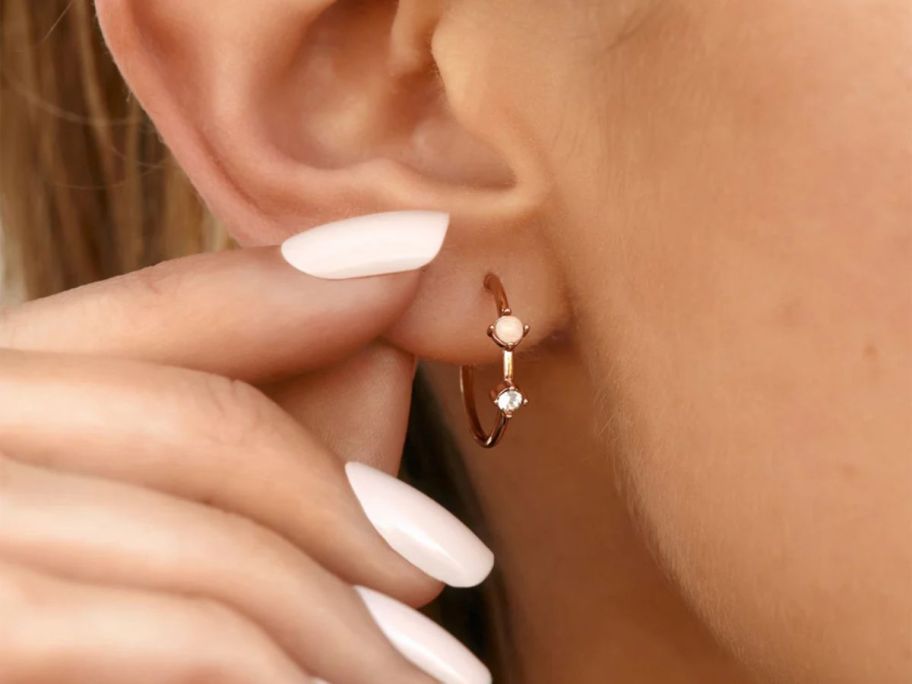 a womans fingers shown grasping her earlobe to show a hoop earring.