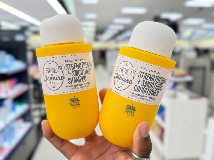 hand holding up yellow Sol de Janiero shampoo & conditioner bottles