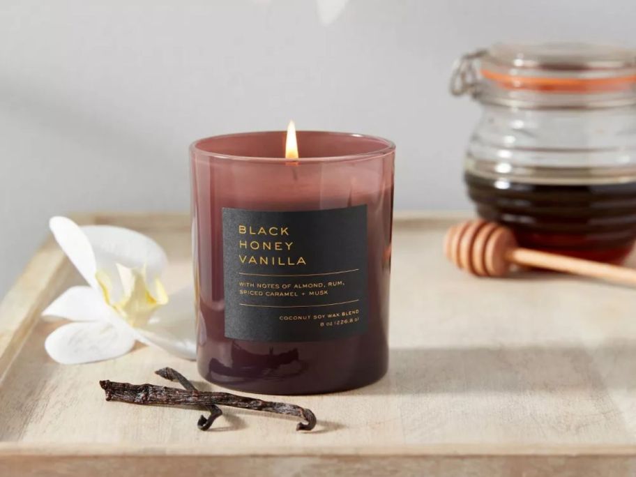 a candle lit on a tabletop next to dried vanilla beans and flowers