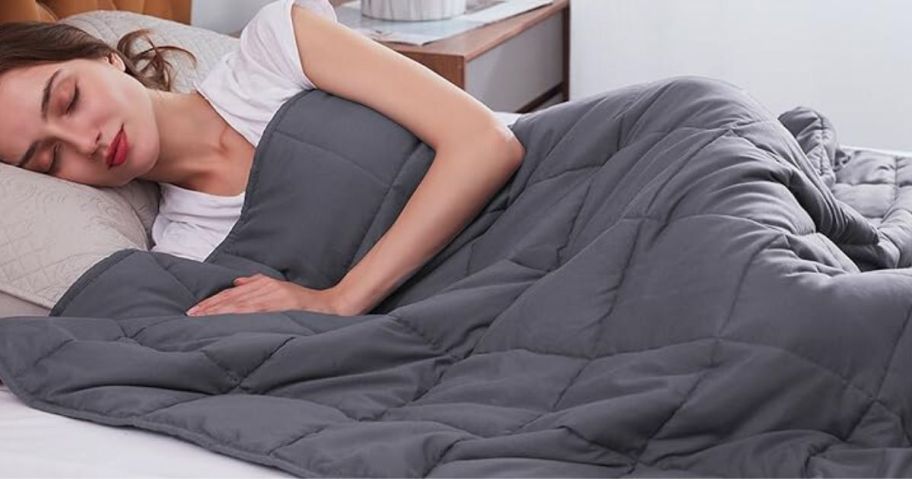 A woman lying down in bed with a grey, weighted blanket