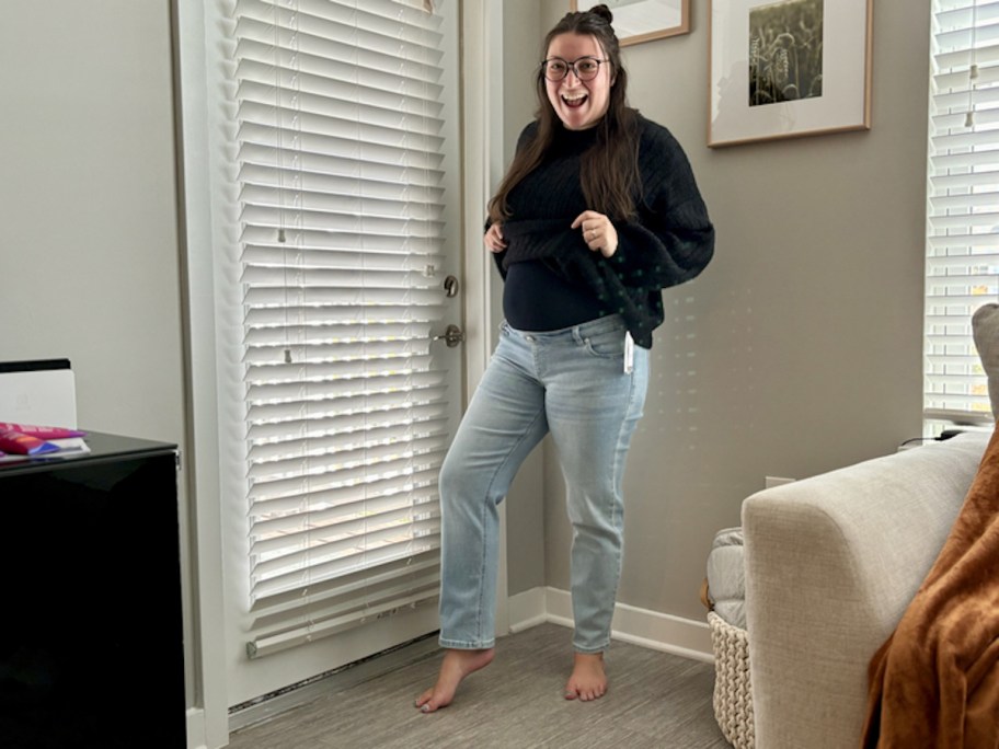 Woman showing off maternity jeans and wearing black sweater 