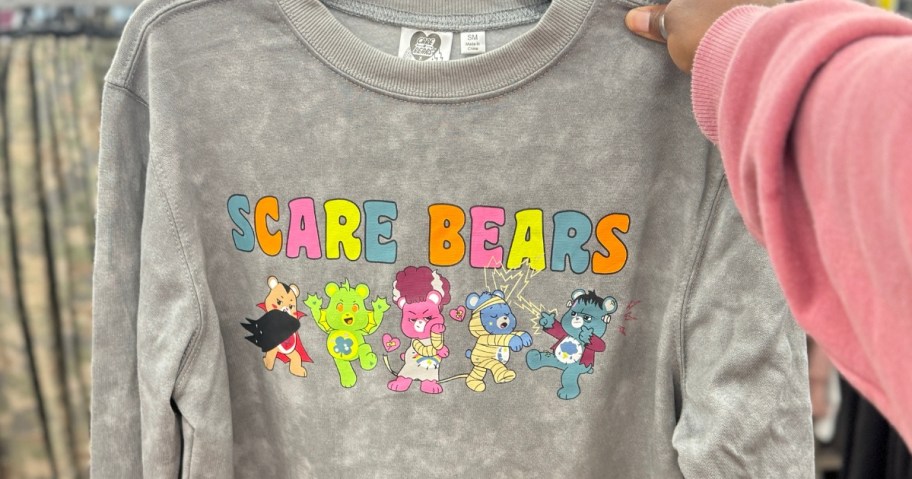 hand holding a grey wash women's sweatshirt with Care Bears Halloween bears on it, that says "Scare Bears"