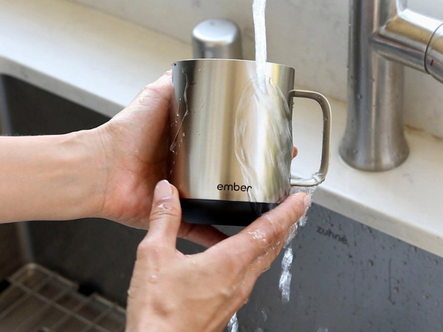 hands holding stainless steel mug being rinsed off under water