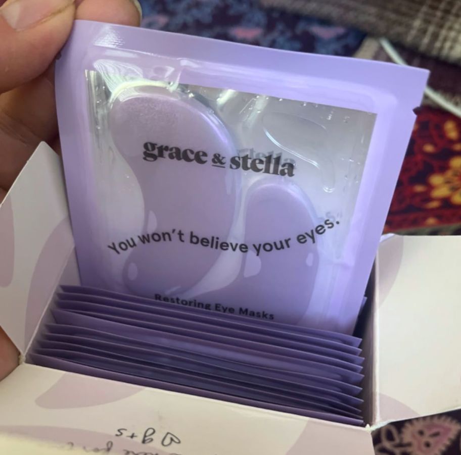 hand pulling a pack of purple Grace & Stella eye masks from a box