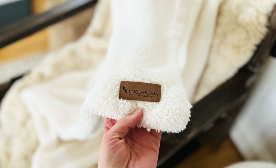 a womans hand holding the corner of a sherpa blankets displaying the item tag.