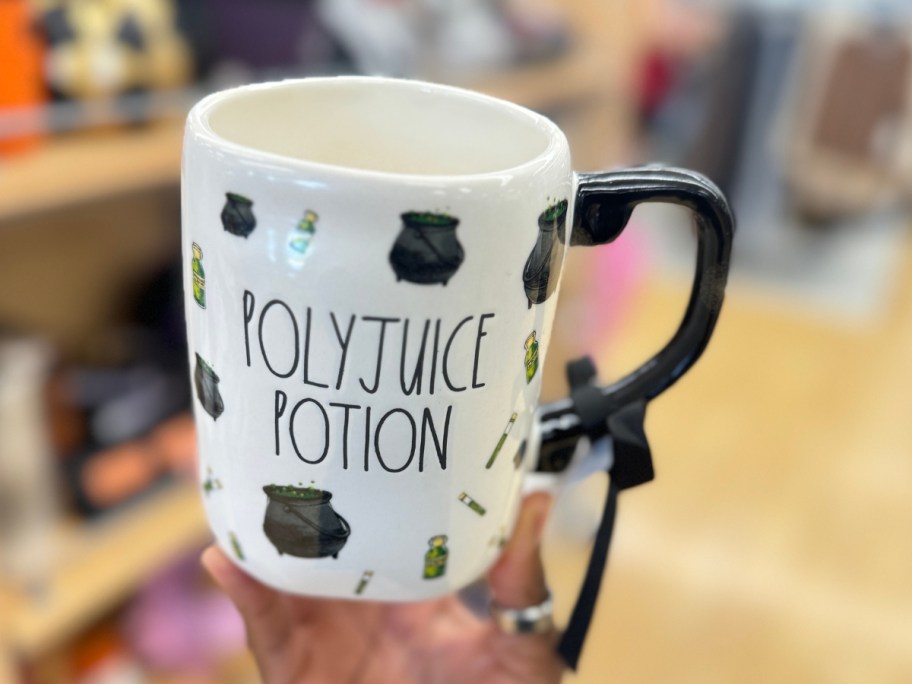 hand holding a coffee mug with various magical items on it that says "Polyjuice Potion"