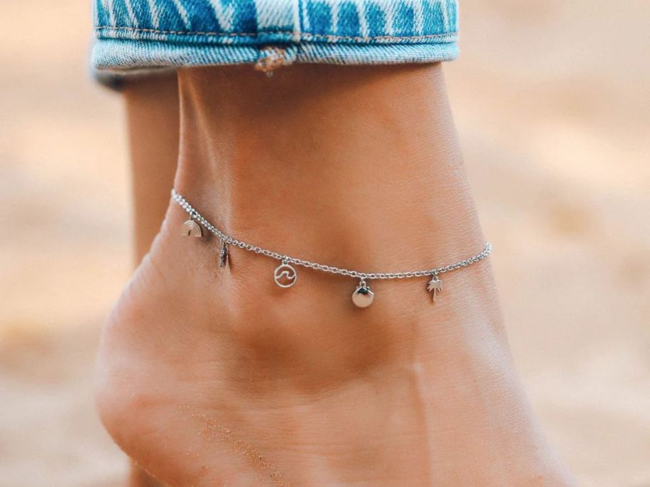 a womans ankle shown with a silver beach themed charm anklet