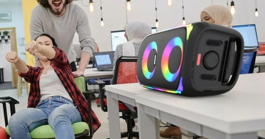 people in an office listening to music on a large black speaker with LED lights that's on it's side on a table