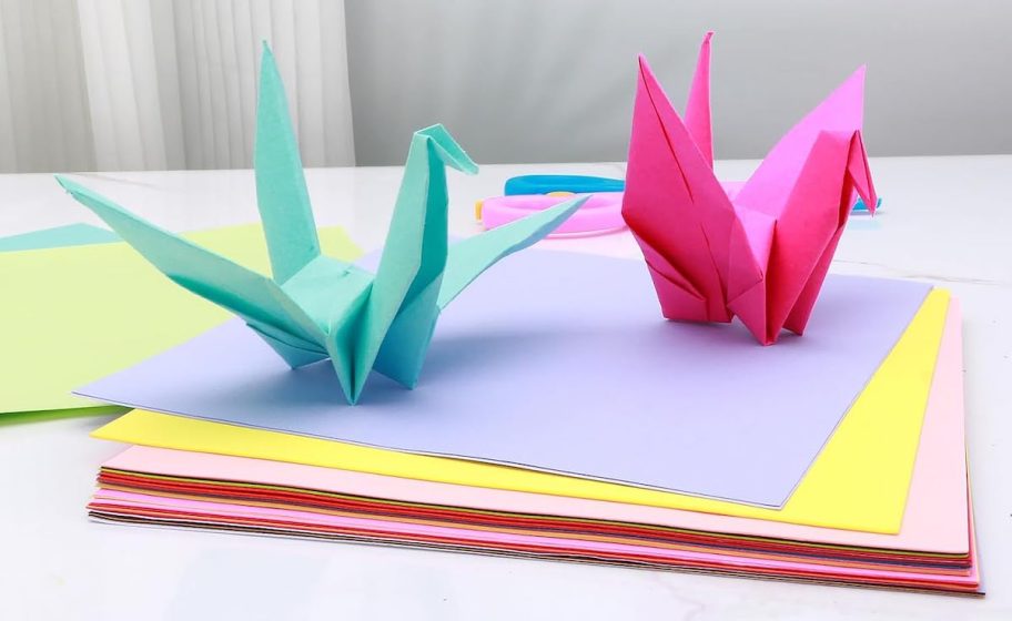 blue and pink origami birds on top of stack of colorful papers