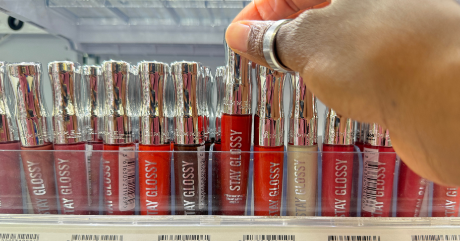 hand grabbing rimmel Stay Glossy Lip Gloss in store from shelf