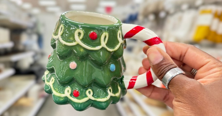 hand holding a Christmas tree shaped coffee mug with a red and white candy cane stripe handle