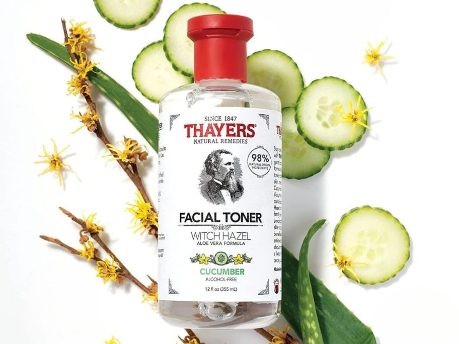Thayers Witch Hazel in Cucumber 12oz bottle on top of cucumbers, aloe, and witch hazel