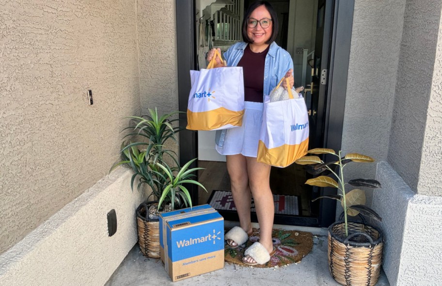 smiling woman wearing slippers and holding up a walmart plus delivery she's collecting from her doorstep