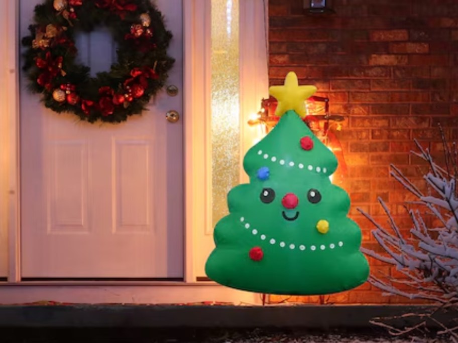 an inflatable small smiling Christmas tree by a home's front door