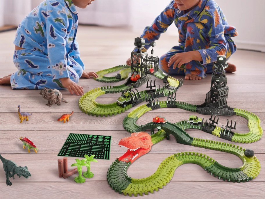 little boys playing with a green and orange dinosaur race track toy