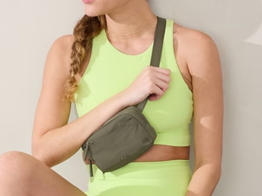 woman in a yellow sports bra and shorts with a greenish tan belt bag worn as a crossbody bag