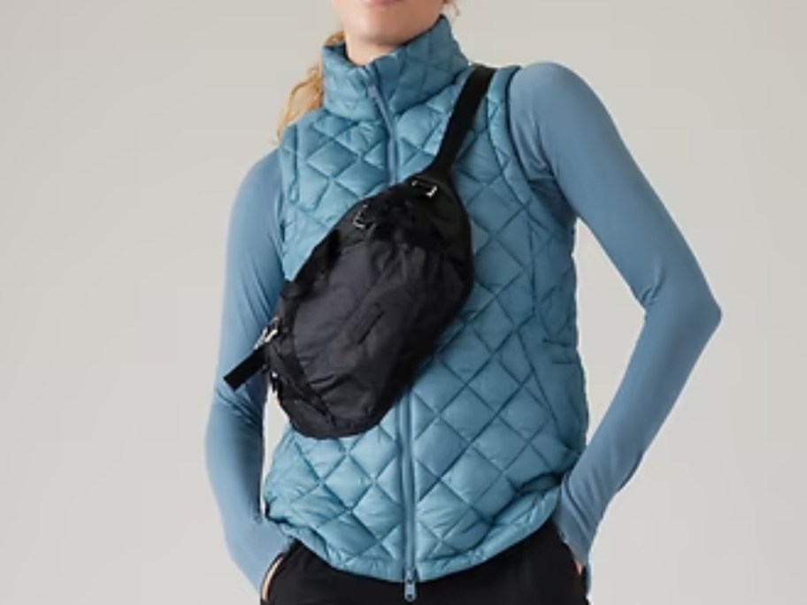 woman wearing a blue quilted jacket and black pants with a large black belt bag worn as a crossbody bag