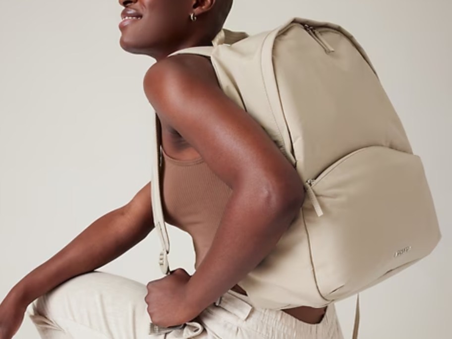 woman crouched down wearing a cream tank top and pants with a cream large backpack on her back