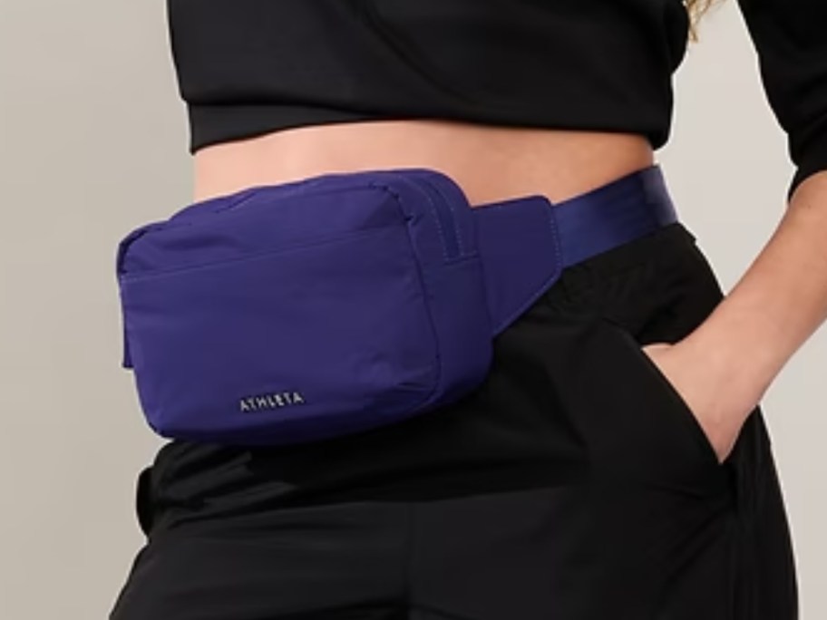woman wearing a black crop top and pants with a royal blue belt bag