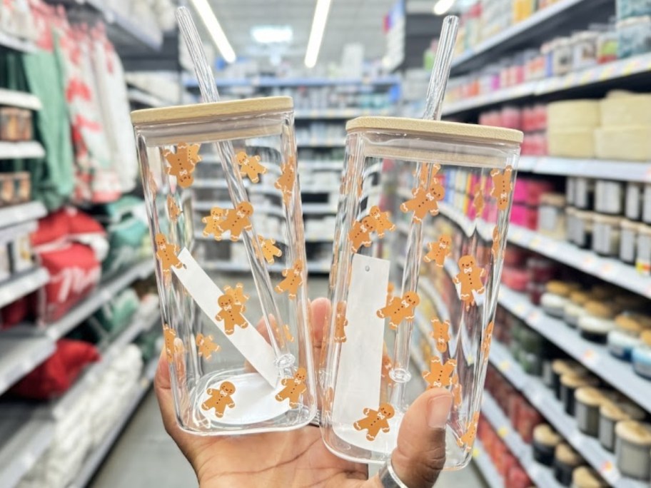 hand holding two square glass tumblers with Gingerbread men on them and bamboo lids and glass straws