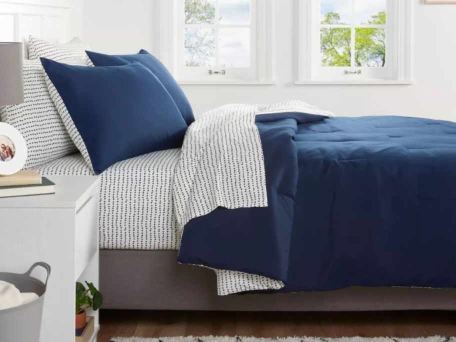 bed with blue and white sheets and a navy blue comforter and pillow shams on it