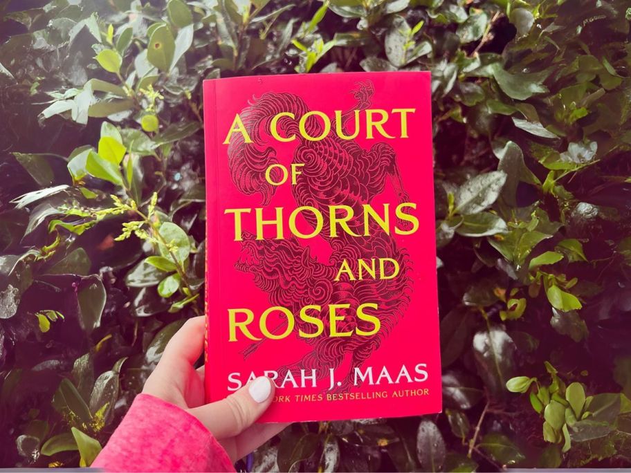 hand holding A Court of Thorns & Roses in front of bush