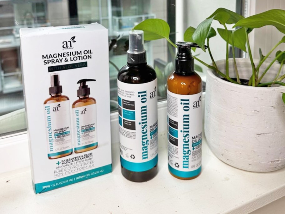 ArtNaturals Magnesium Oil spray and lotion bottles with their box on a windowsill near a plant