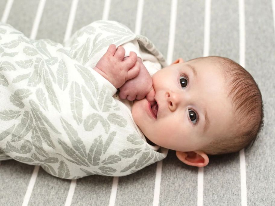 a swaddled baby laying on a Burt's Bees sheet