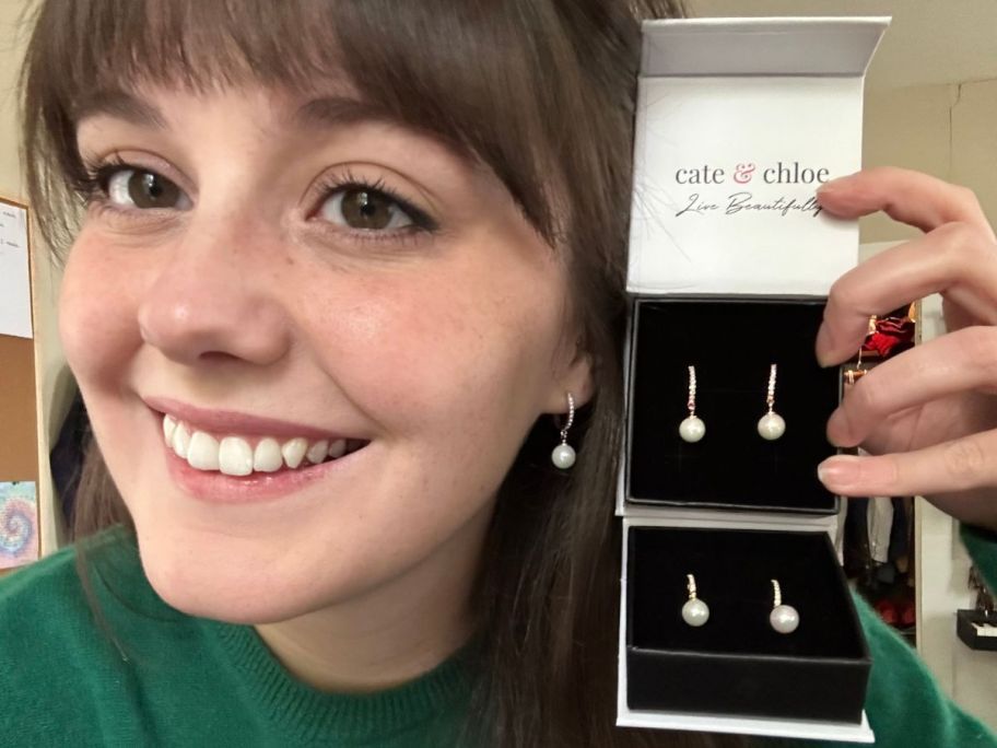 Woman holding two boxes with Cate & Chloe Daphne Earrings next to her face while wearing the Daphne Earrings