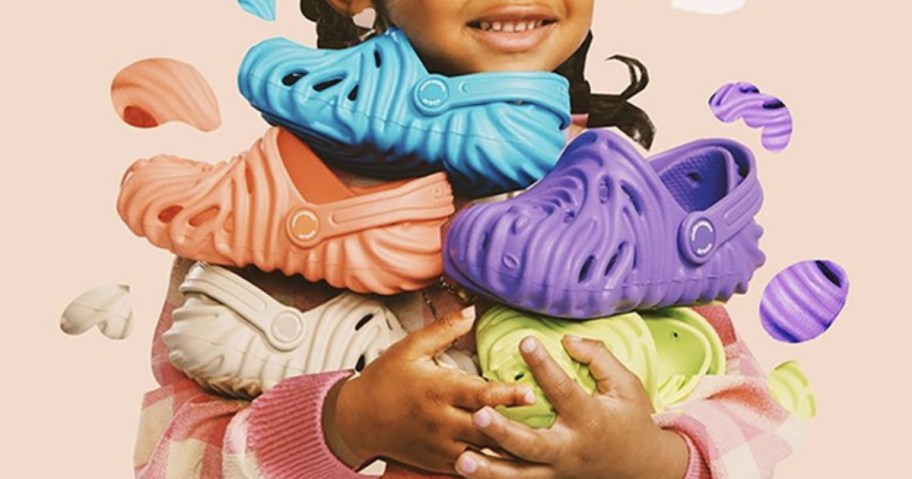 little girl holding a bunch of Crocs clog shoes in bright colors with a ridged swirly pattern design