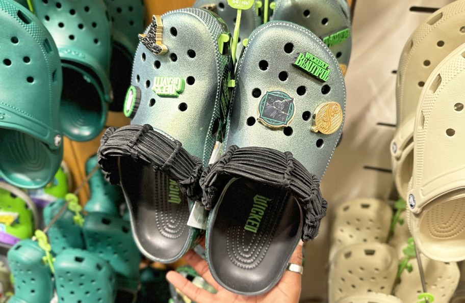 hand holding a green and black pair of crocs with Wicked charms