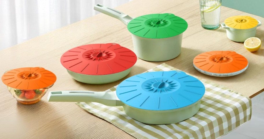 set of pots, pans, and bowls with colorful silicone lids on top on a kitchen table