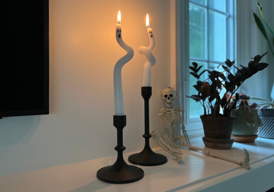 white ghost taper candles in black holders on mantle next to plants