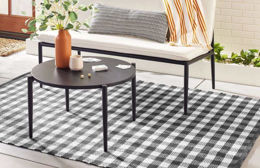 a gray and white gingham area rug on a patio shown with an outdoor sofa and table