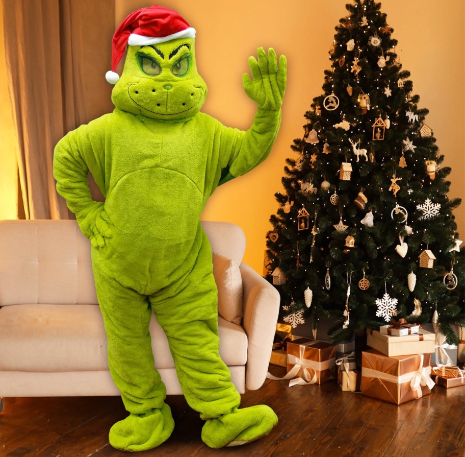 person in a grinch costume standing next to a christmas tree